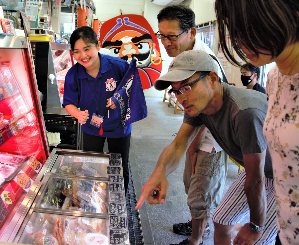 市場のお店でガイドの案内を聞き、ショーケースを指さす参加者たち